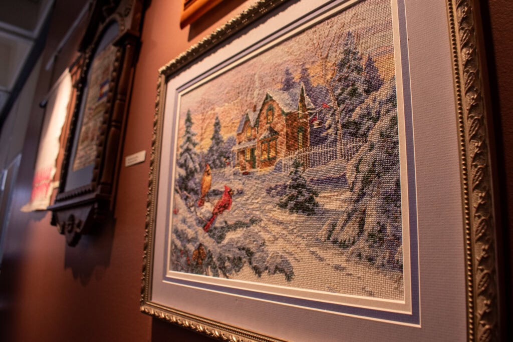 framed cross stitch piece depicting a snowy cabin in the woods