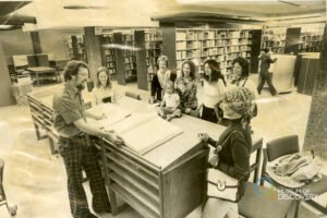 Library employee (Larry Webber) talking to a group of women and children in the library