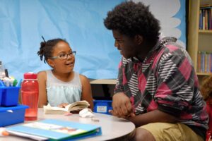 teen boy and young girl reading together at a library