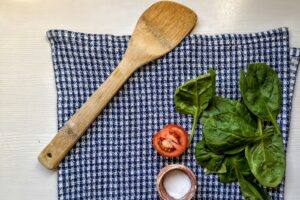 tomato, spinach, salt, and wooden spoon on a kitchen towel