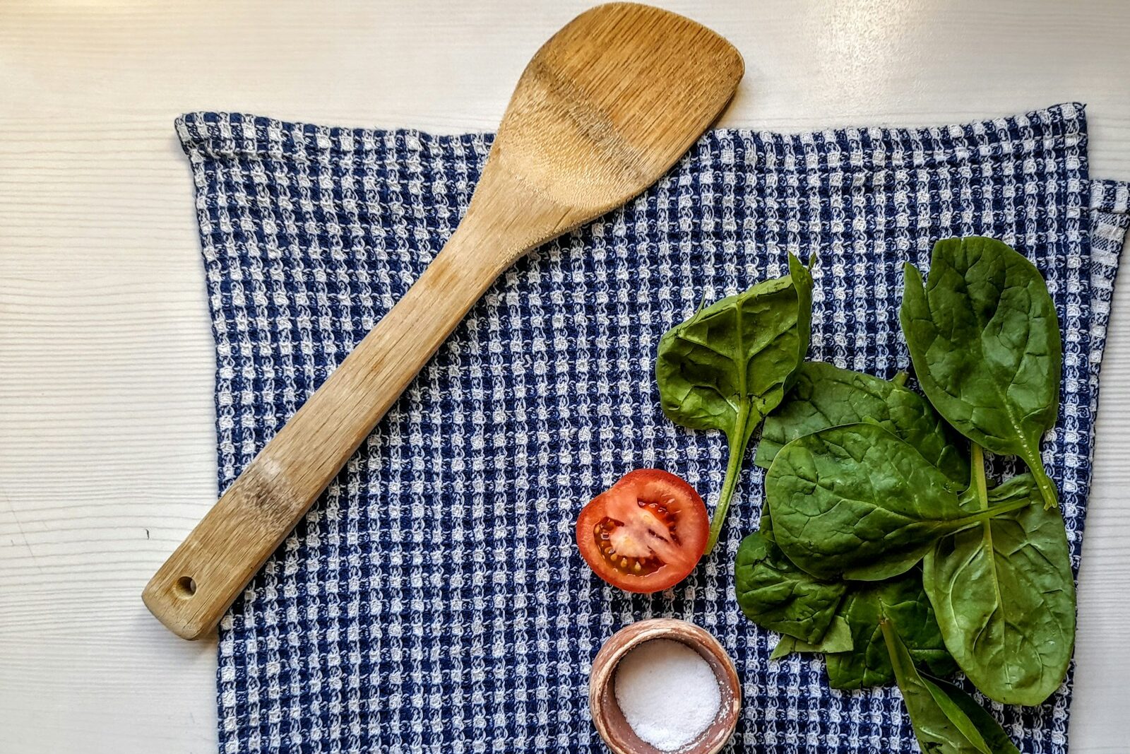 tomato, spinach, salt, and wooden spoon on a kitchen towel
