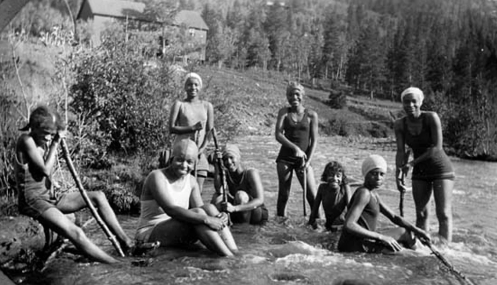 Grupo de jóvenes afroamericanas sonriendo para una foto mientras nadan en un lago.