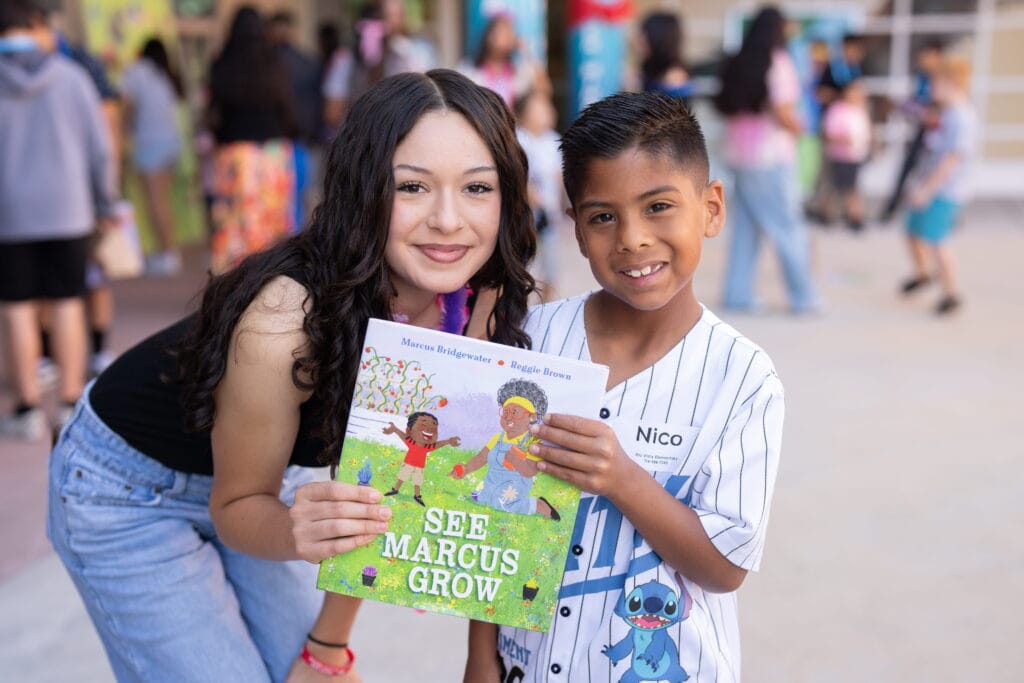 teenage girl and young boy smiling for photo while holding up a book