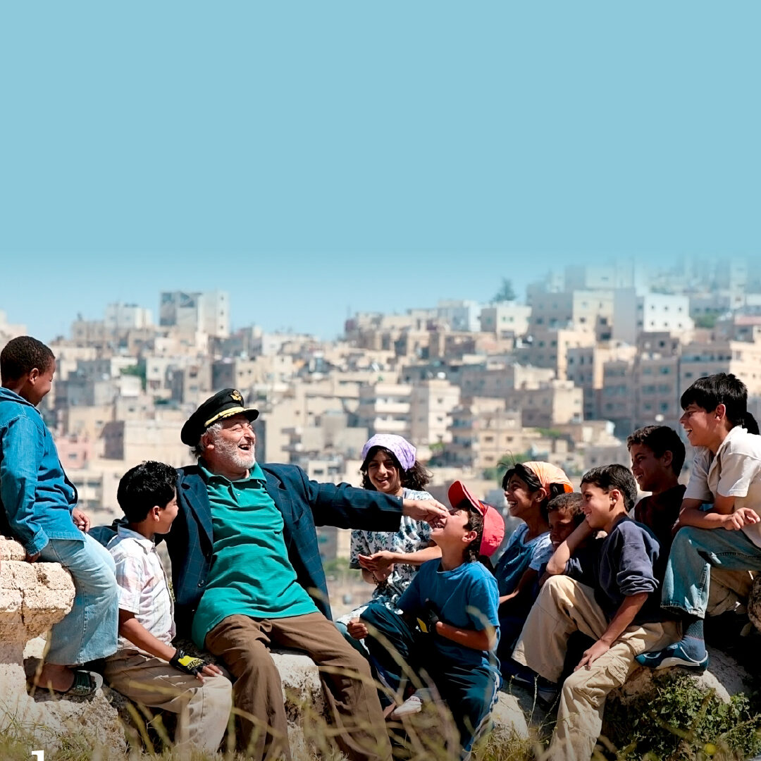 older man laughing and talking to a group of children