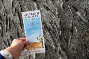 hand holding up a summer adventure bookmark in front of a rock with fossils in it