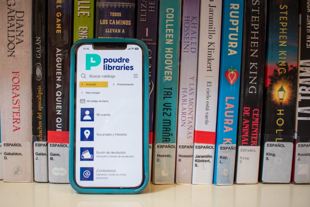 aplicación de bibliotecas poudre en un teléfono móvil posicionado frente a libros