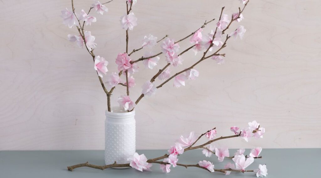 ramas de cerezo de papel en un jarrón blanco sobre una mesa