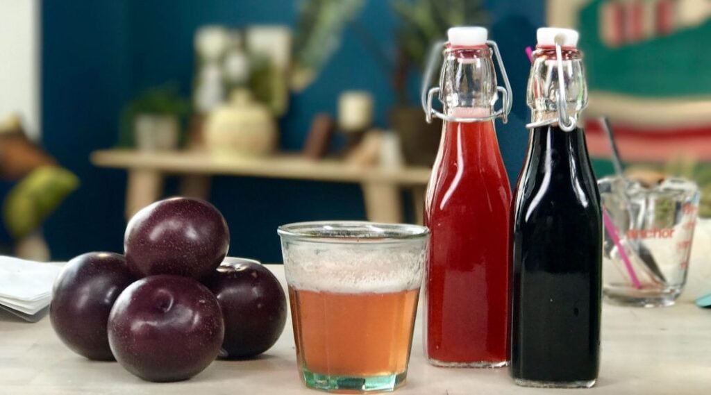 ciruelas, un vaso y recipientes de bebidas coloridas sobre una mesa juntos