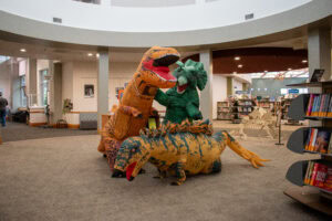 a t-rex, stegasaurus, and triceratops in a library