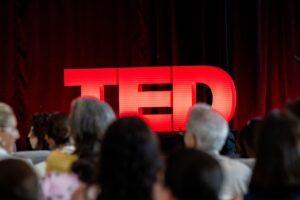 people seated in front of a stage with a red TED sign